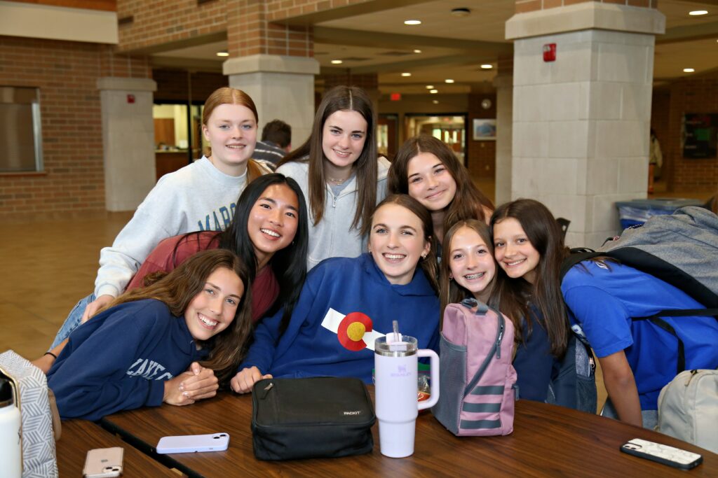 group of girls huddled together smiling at camera in cafeteria